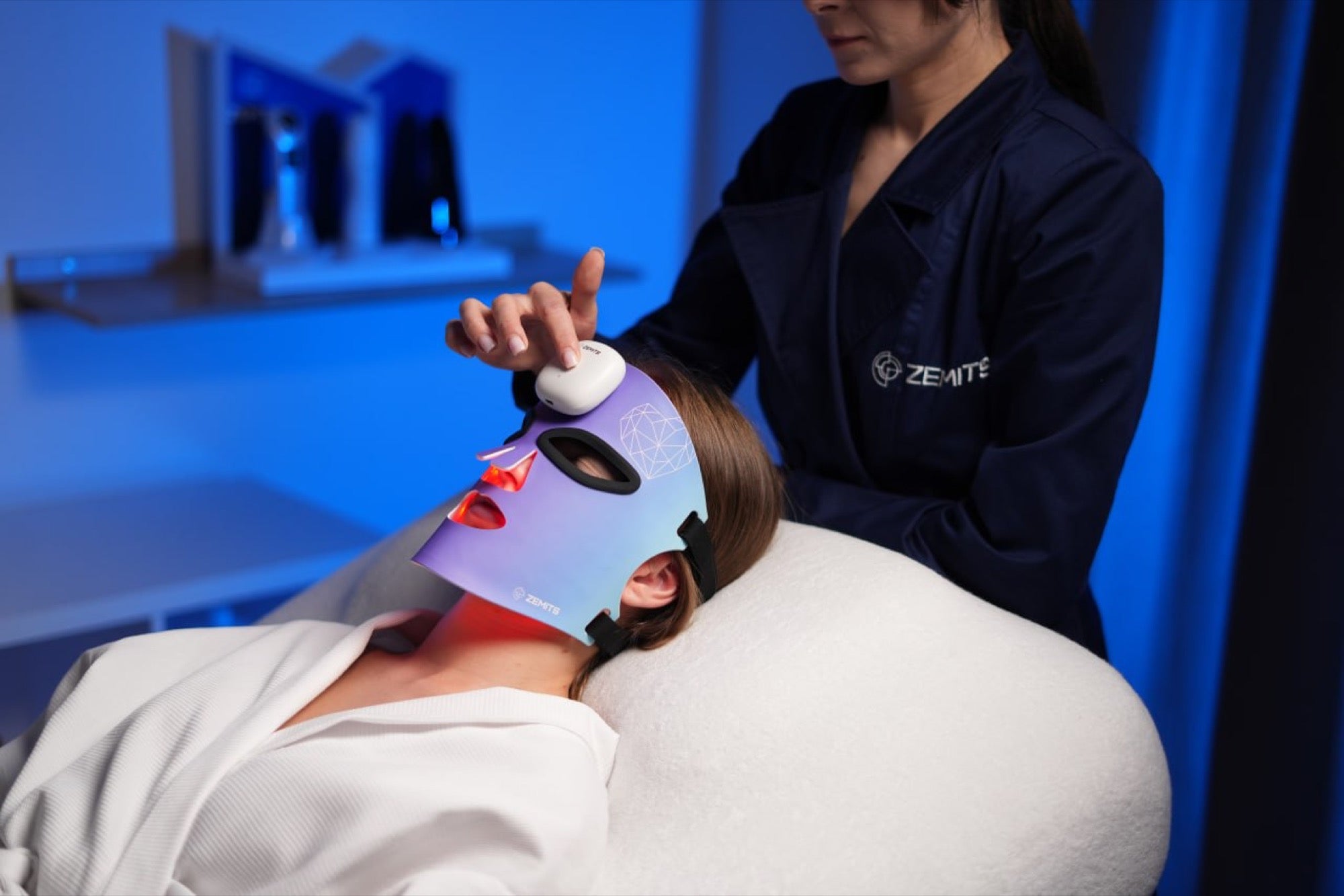 An esthetician adjusts the Zemits MaiSkin LED mask on a client during a professional treatment