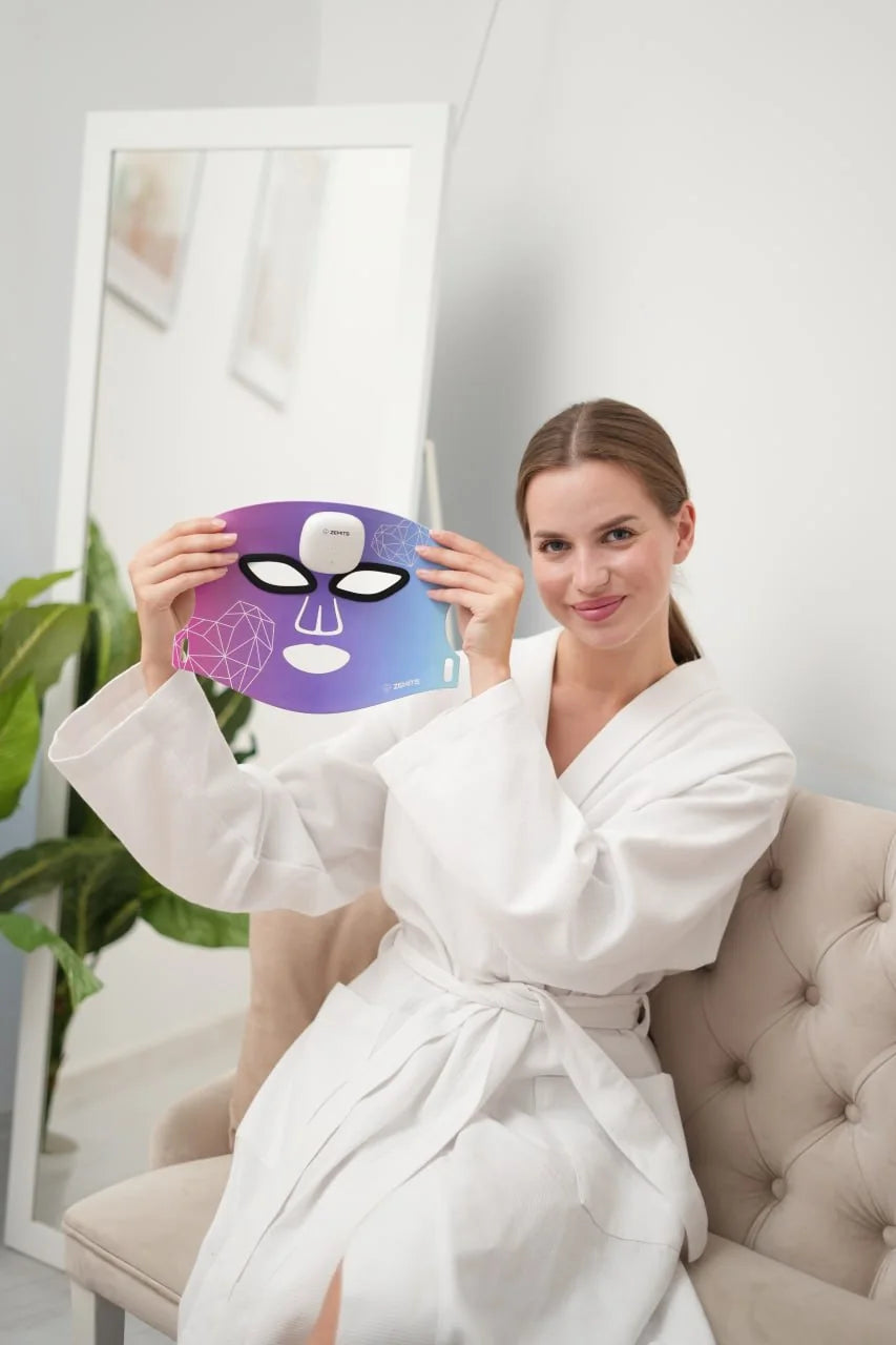 A woman in a white robe holding the Zemits MaiSkin mask as part of her home skincare routine
